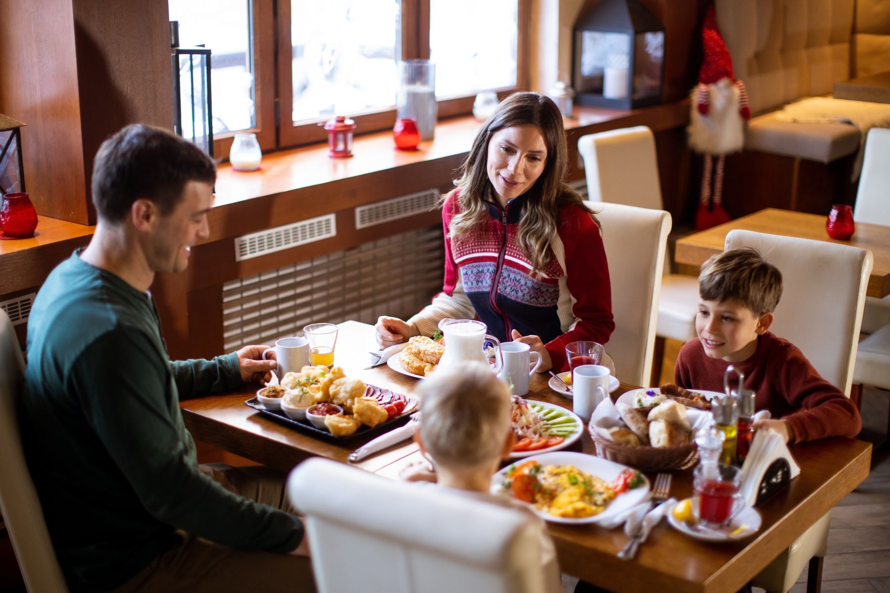 A family of four shares a breakfast at a wooden table, with croissants, fruit, and drinks spread across the table in a cozy dining room.